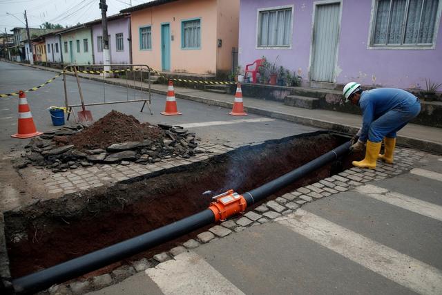 Abertura de vala para implantação de rede de abastecimento de água em rua de casas coloridas.